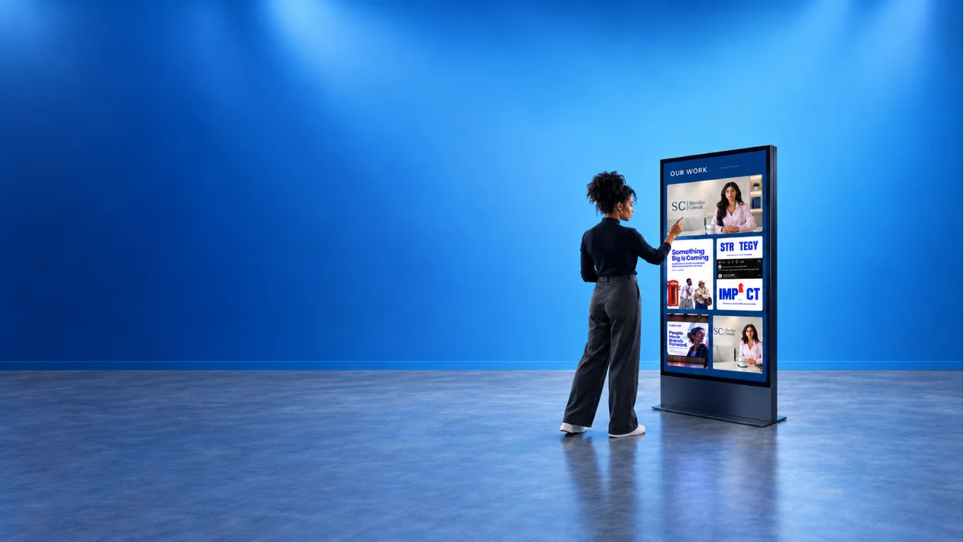 Woman using a large touchscreen kiosk showing Quantum's Our Work portfolio in a bright blue room.